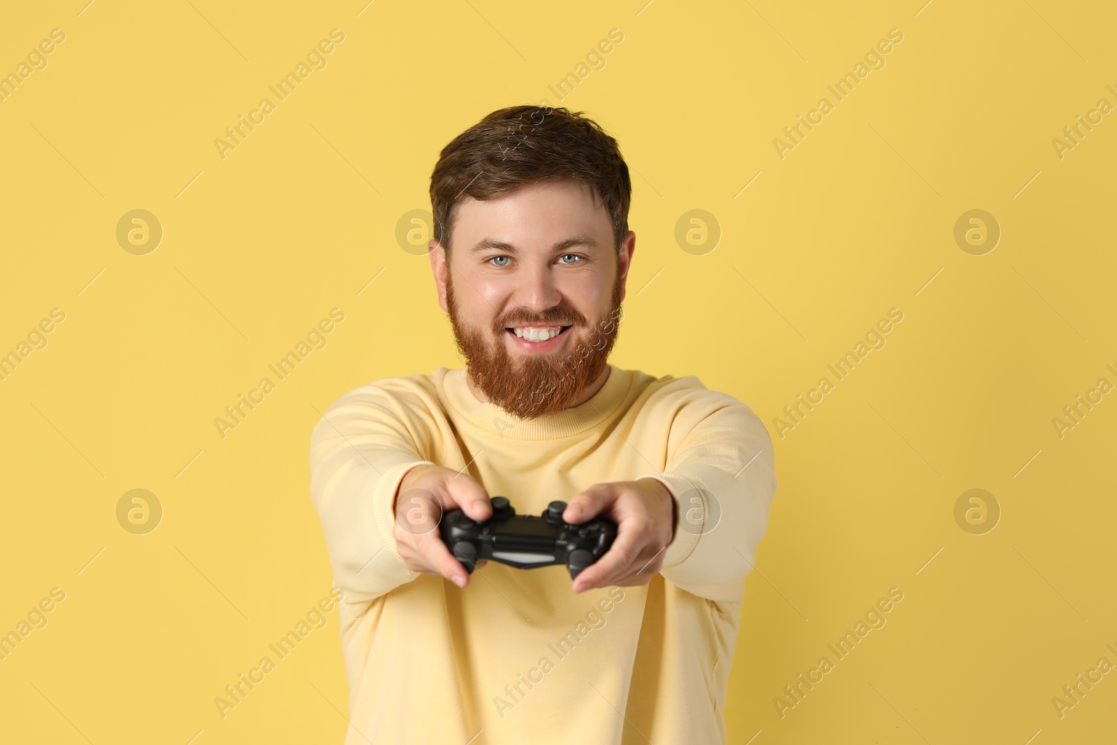 Photo of Happy man with game controller on pale yellow background