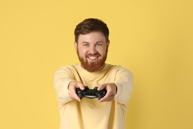 Photo of Happy man with game controller on pale yellow background
