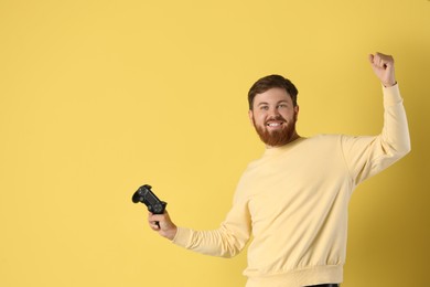 Photo of Happy man with game controller on pale yellow background. Space for text