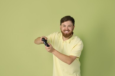 Photo of Happy man playing video game with controller on pale green background