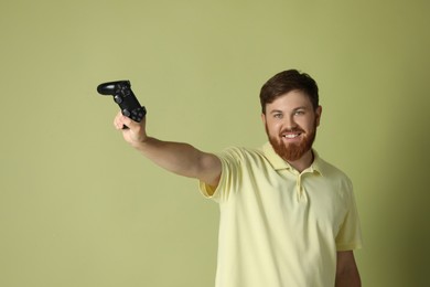 Smiling man with game controller on pale green background