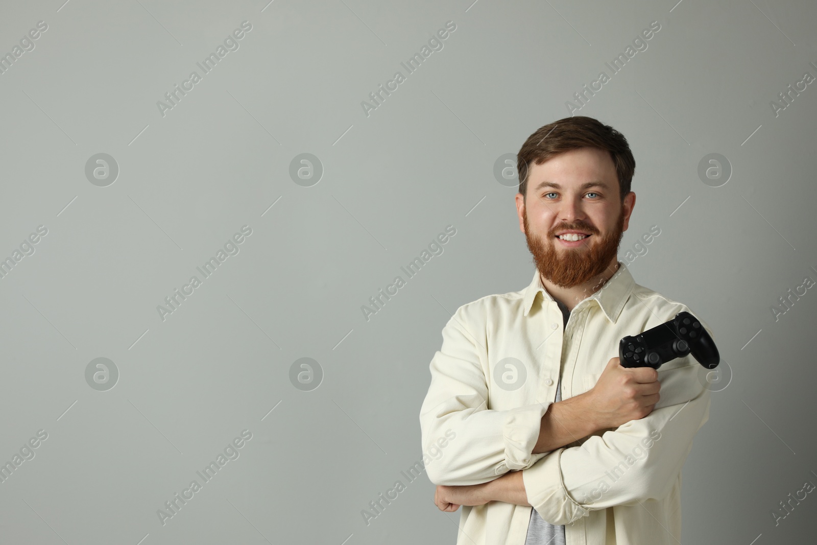 Photo of Smiling man with game controller on grey background. Space for text