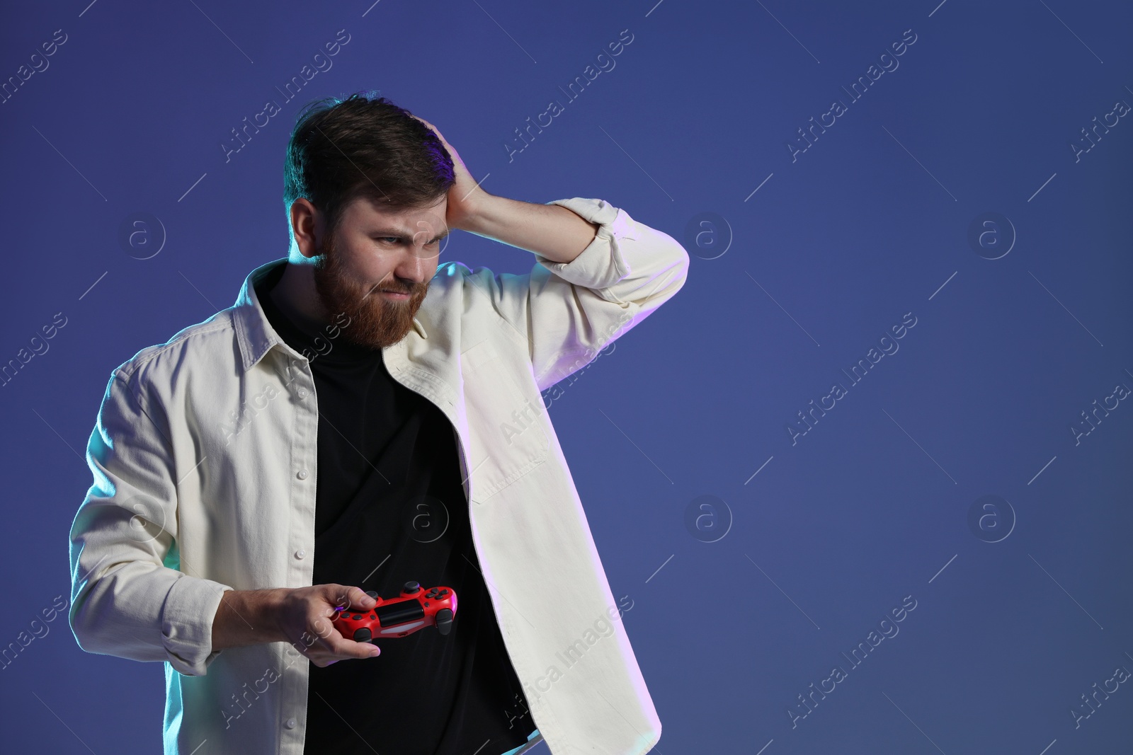 Photo of Sad man with game controller on dark blue background. Space for text