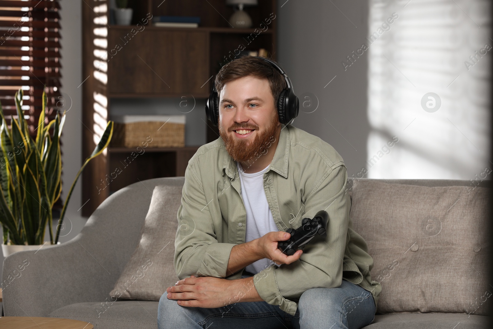 Photo of Happy man in headphones with game controller at home