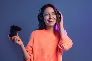 Happy woman in headphones with game controller on dark blue background