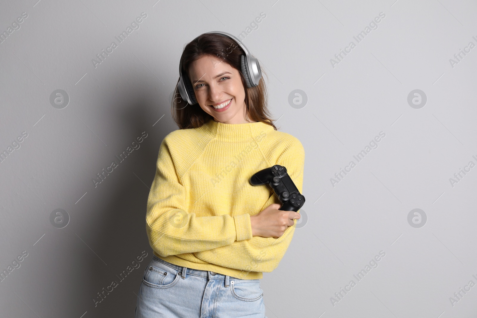 Photo of Happy woman in headphones with game controller on light grey background