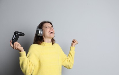 Happy woman in headphones with game controller on light grey background. Space for text