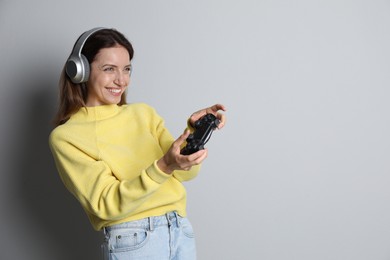 Photo of Happy woman in headphones playing video game with controller on light grey background. Space for text