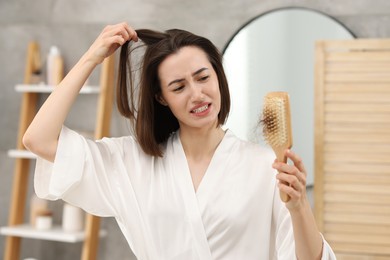 Photo of Emotional woman holding brush with lost hair in bathroom. Alopecia problem