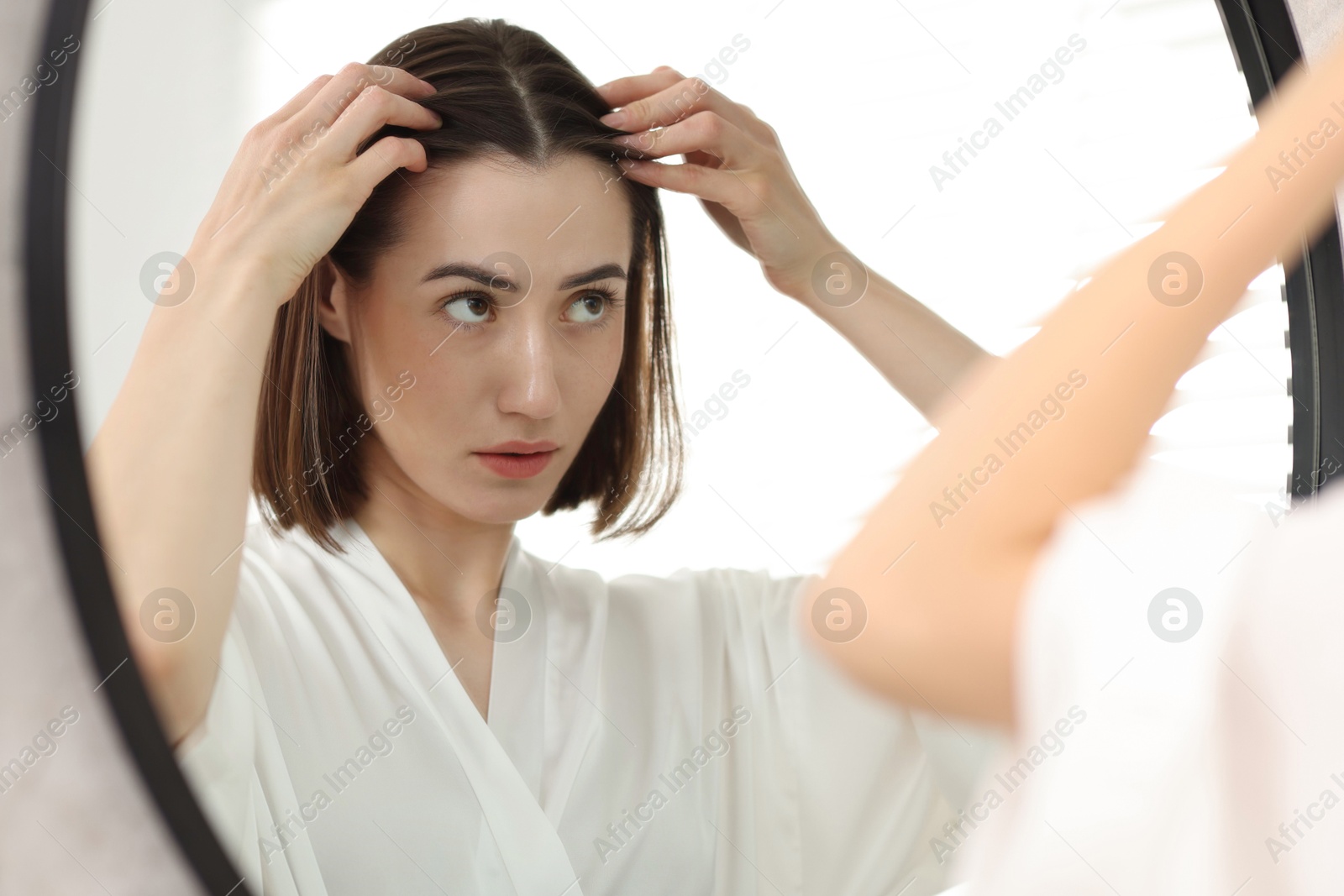 Photo of Young woman with hair loss problem looking at mirror indoors