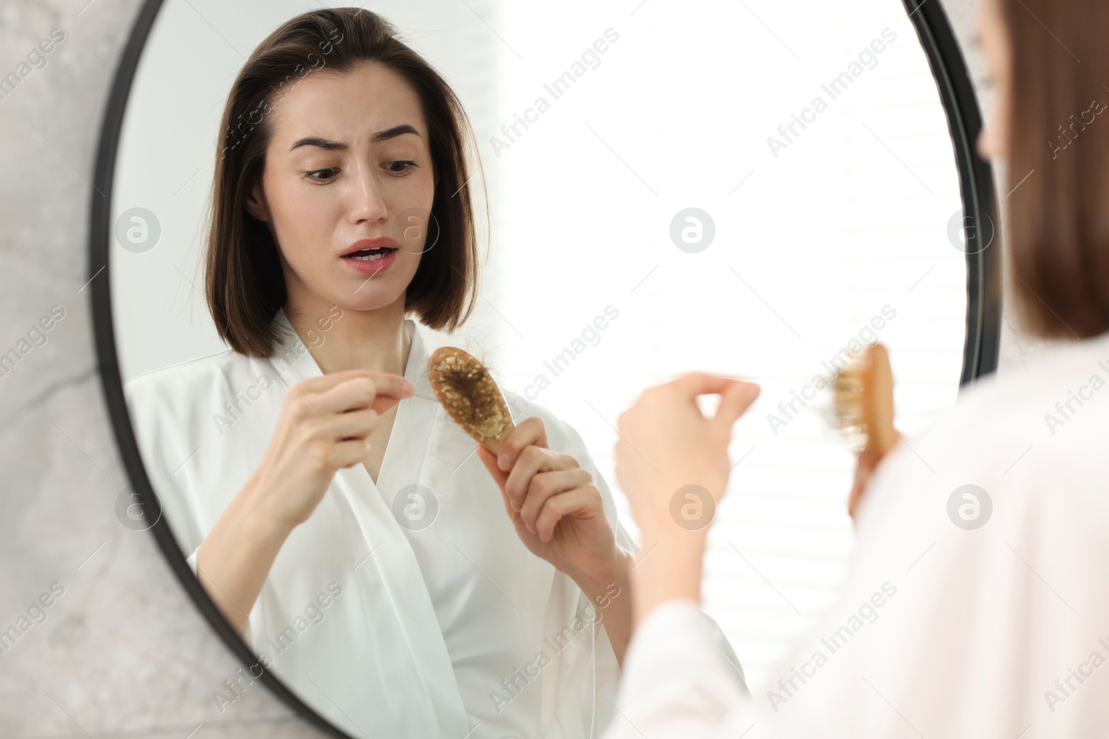 Photo of Emotional woman taking her lost hair from brush in bathroom. Alopecia problem