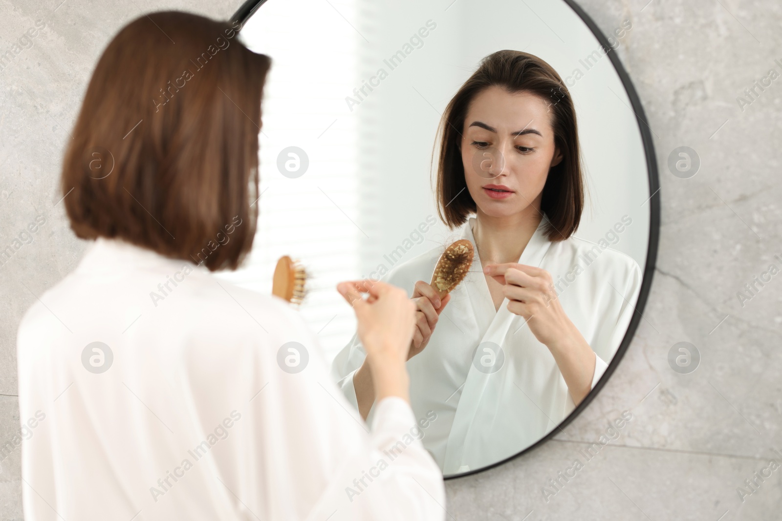 Photo of Sad woman taking her lost hair from brush indoors. Alopecia problem