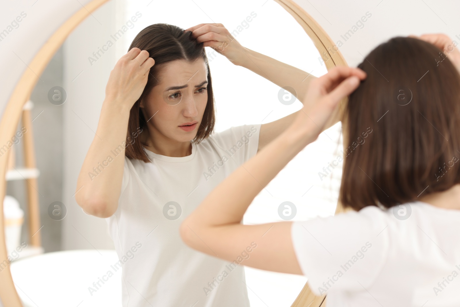 Photo of Sad woman with hair loss problem looking at mirror indoors