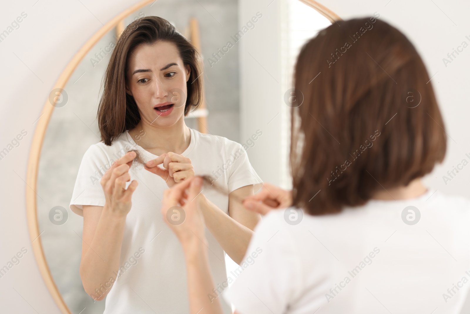 Photo of Emotional woman holding clump of lost hair indoors. Alopecia problem