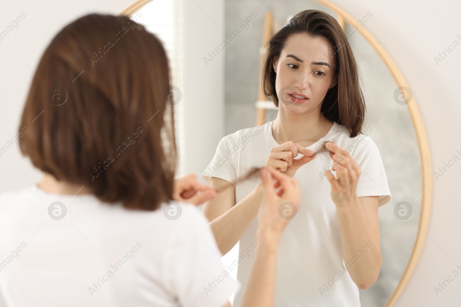 Photo of Stressed woman holding clump of lost hair near mirror indoors. Alopecia problem