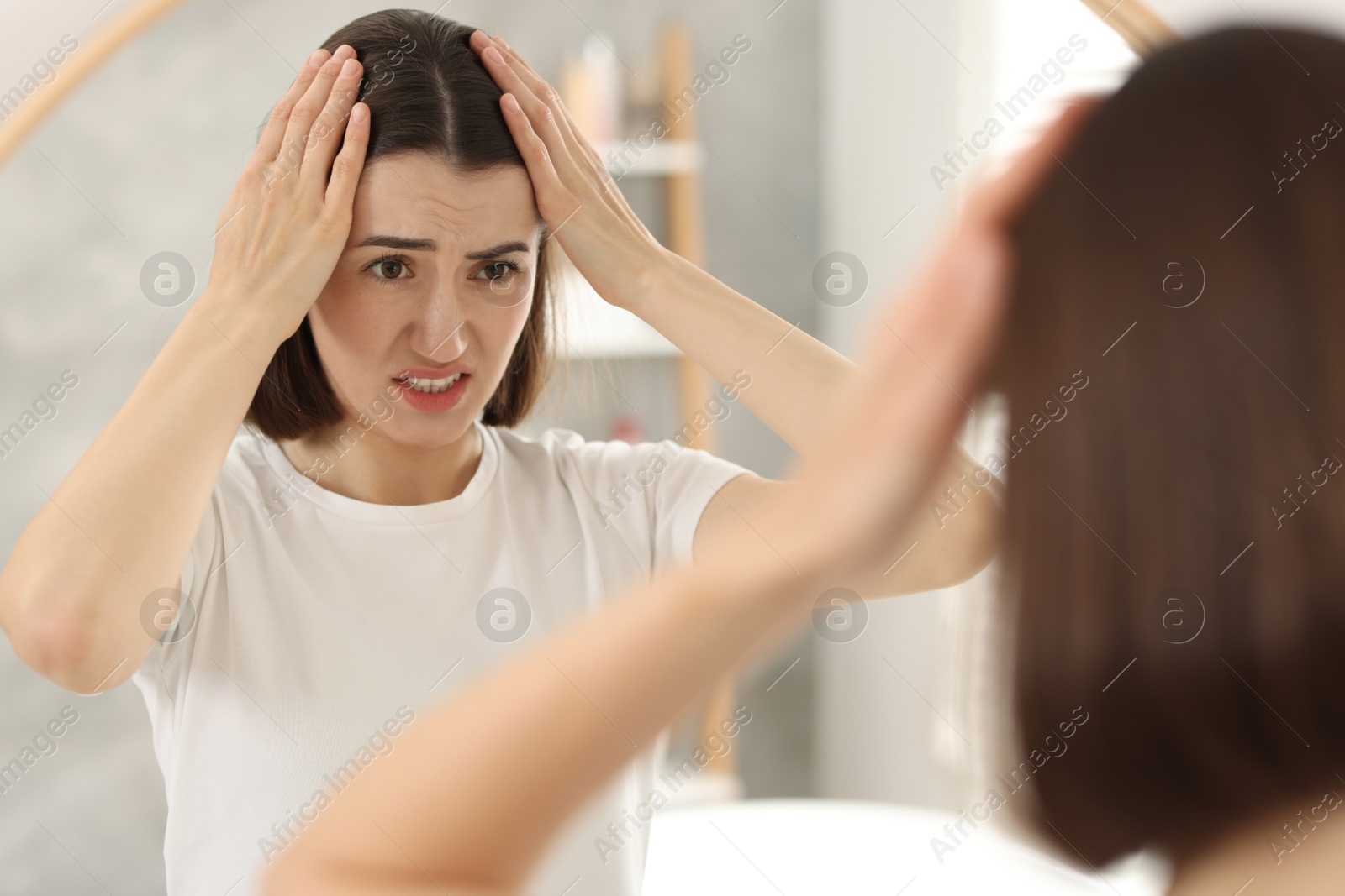 Photo of Sad woman with hair loss problem looking at mirror indoors