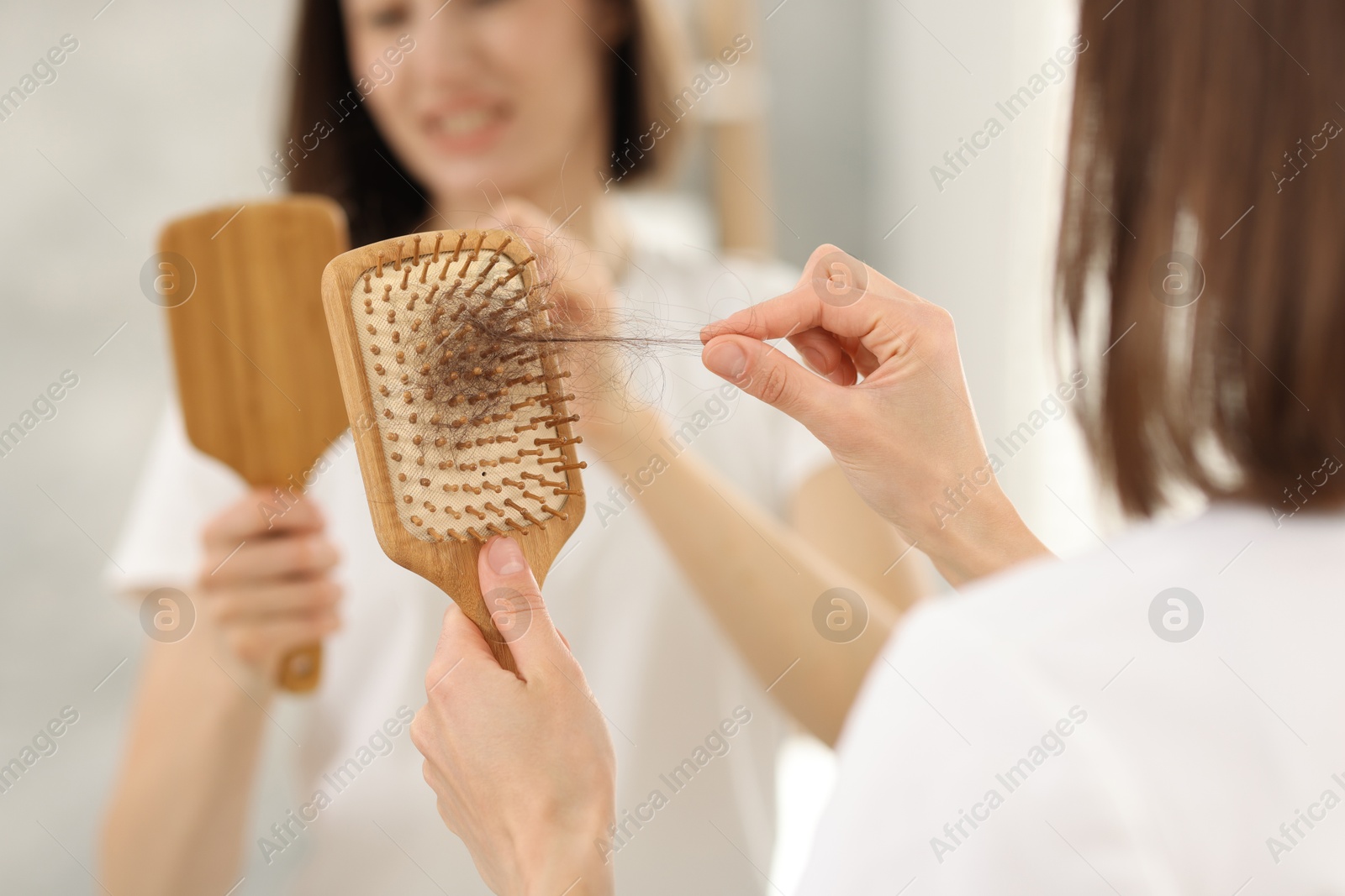 Photo of Woman taking her lost hair from brush near mirror indoors, closeup. Alopecia problem