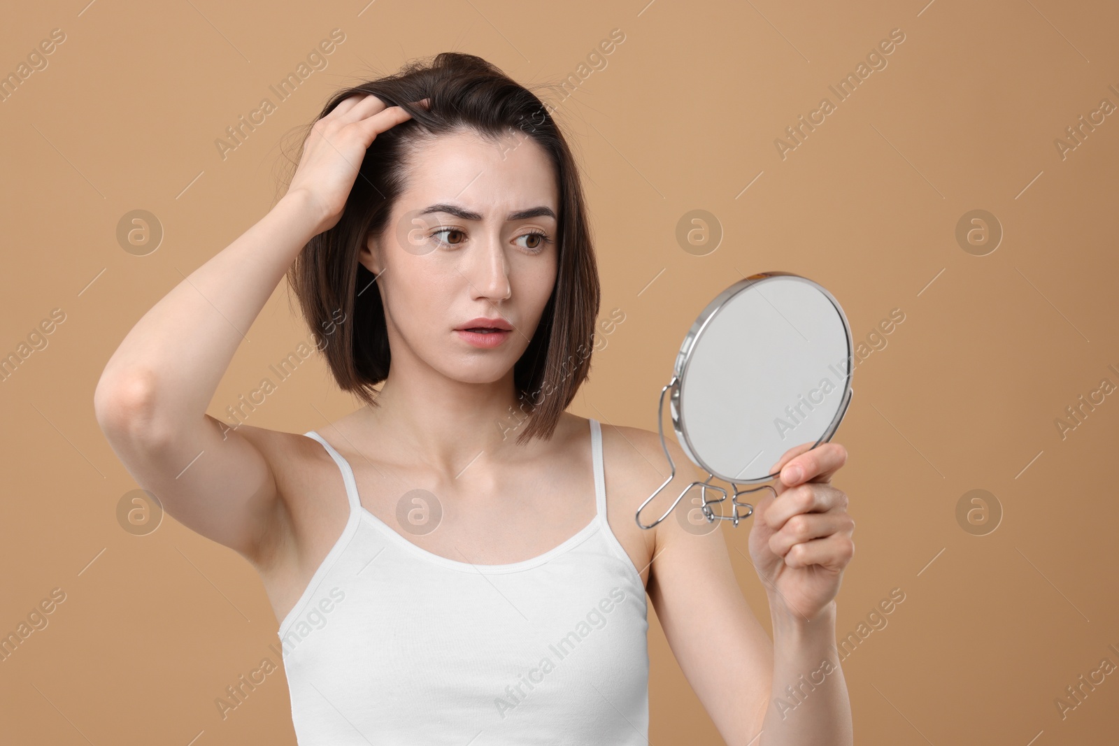 Photo of Sad woman with hair loss problem looking at mirror on light brown background