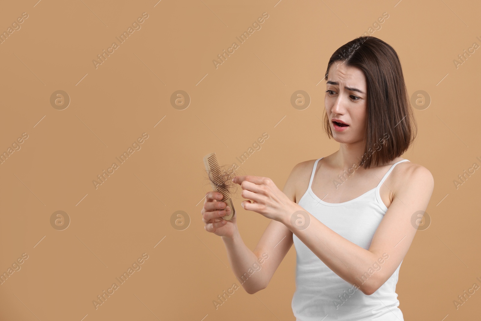 Photo of Emotional woman taking her lost hair from comb on light brown background. Alopecia problem