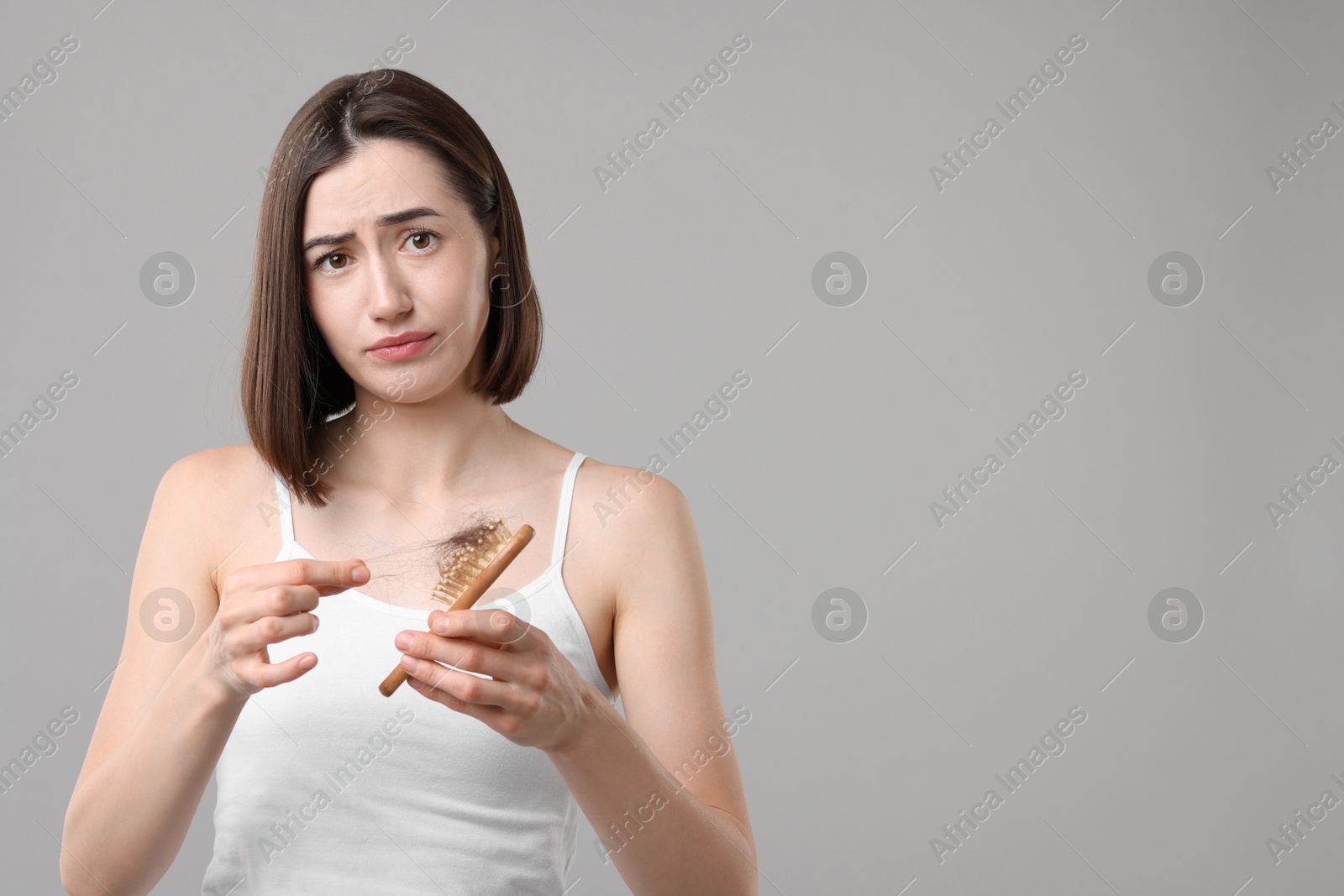 Photo of Sad woman taking her lost hair from brush on grey background, space for text. Alopecia problem