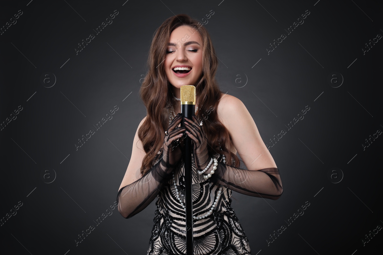 Photo of Beautiful young woman in stylish dress with microphone singing on dark background