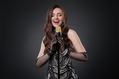 Beautiful young woman in stylish dress with microphone singing on dark background