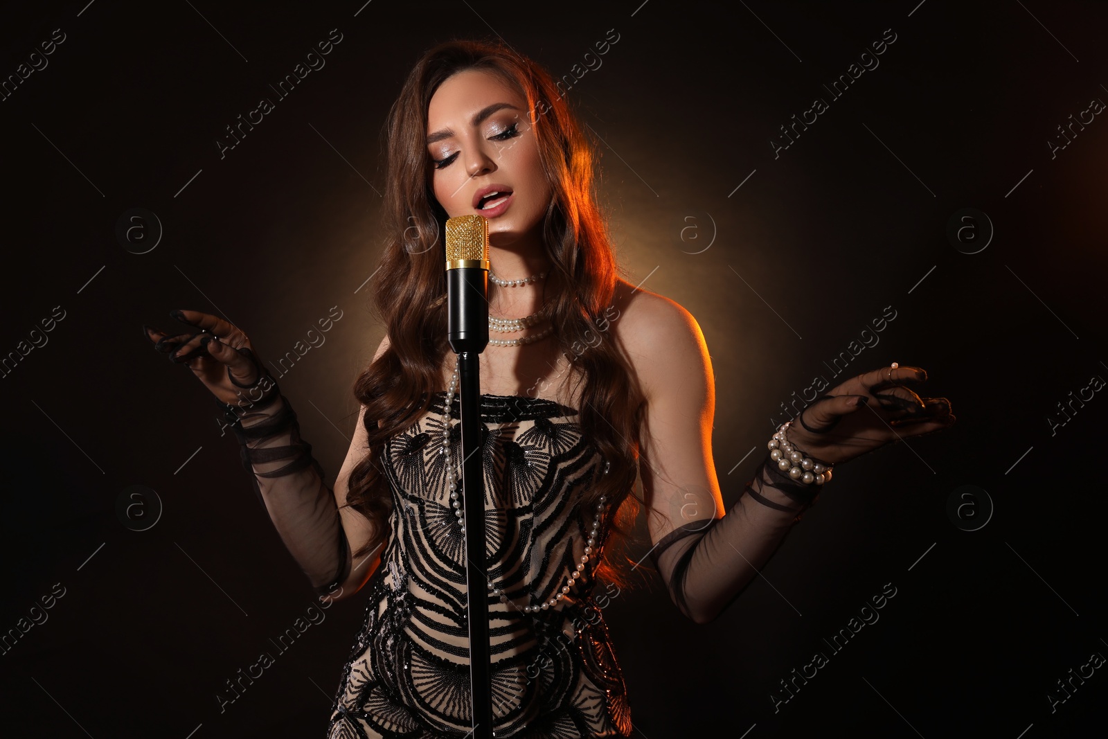 Photo of Beautiful young woman in stylish dress with microphone singing on dark background