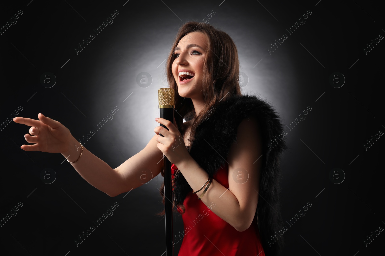 Photo of Beautiful young woman with microphone singing on black background