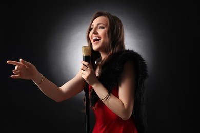 Beautiful young woman with microphone singing on black background