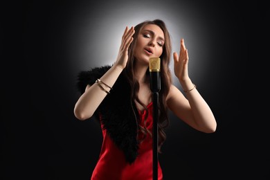 Beautiful young woman with microphone singing on black background