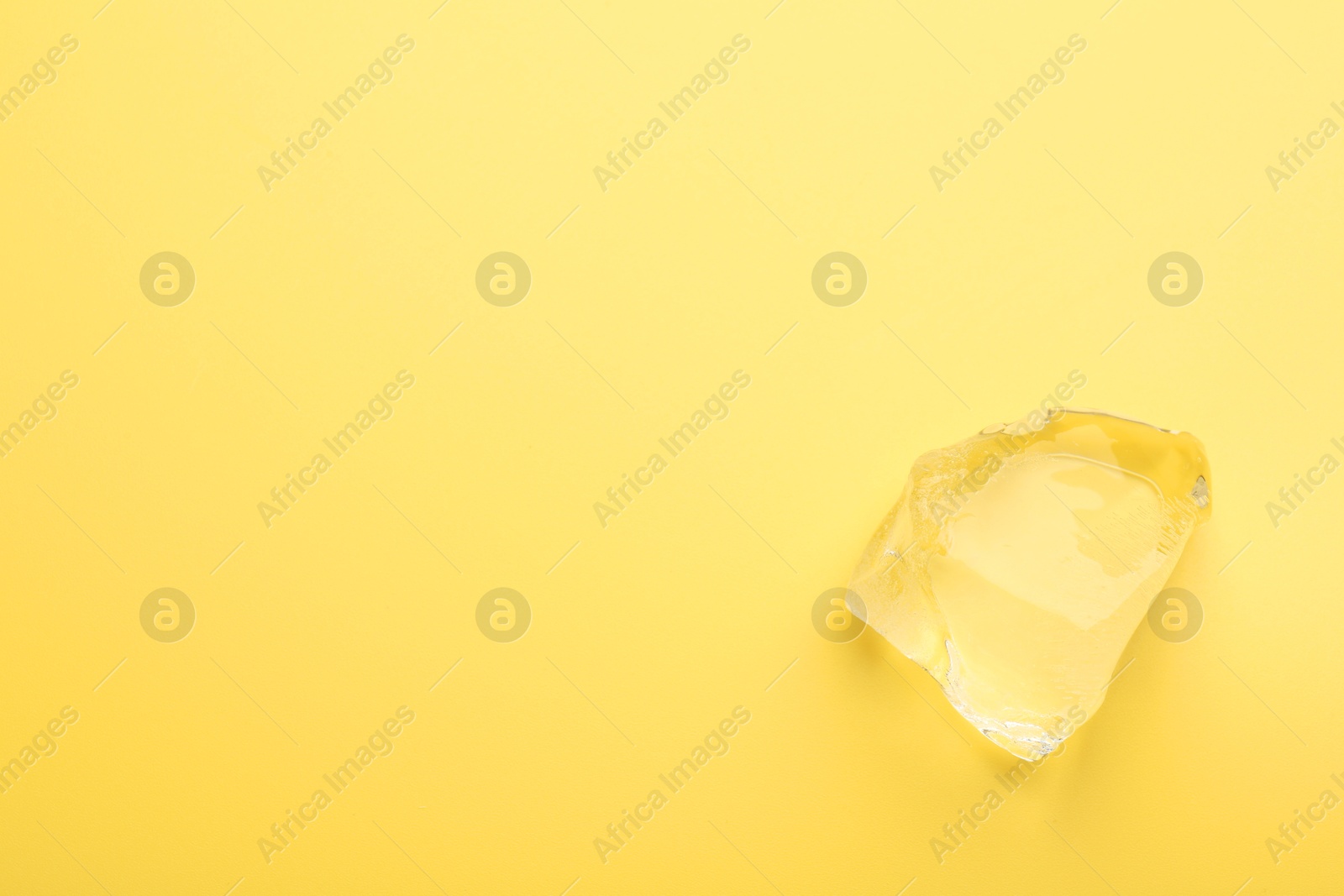 Photo of Piece of clear ice on yellow background, top view. Space for text