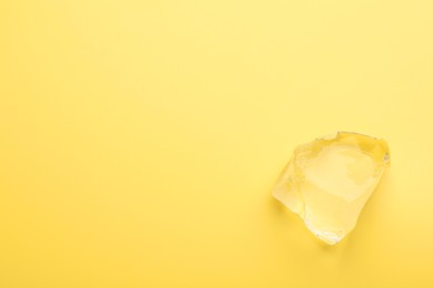 Piece of clear ice on yellow background, top view. Space for text