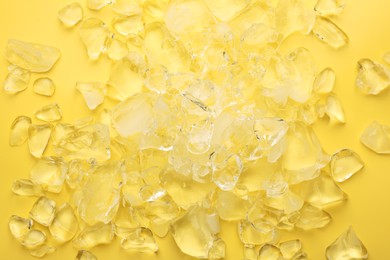 Pieces of crushed ice on yellow background, top view