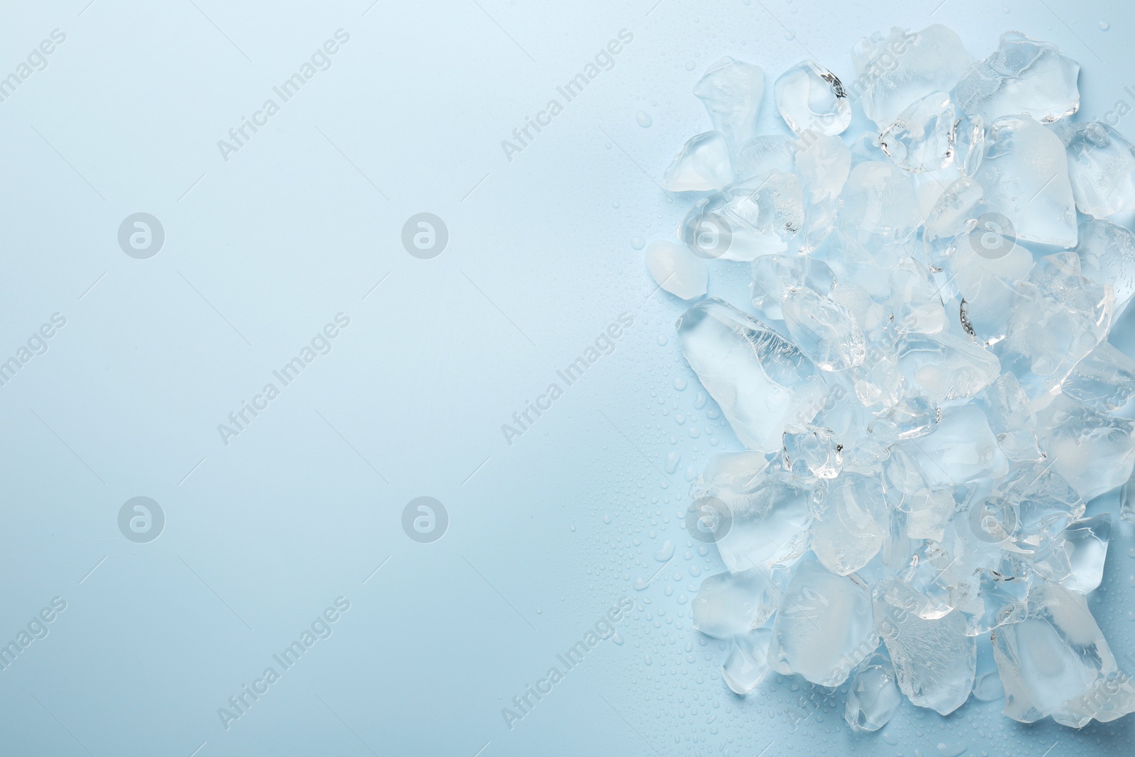 Photo of Pieces of crushed ice on light blue background, top view. Space for text