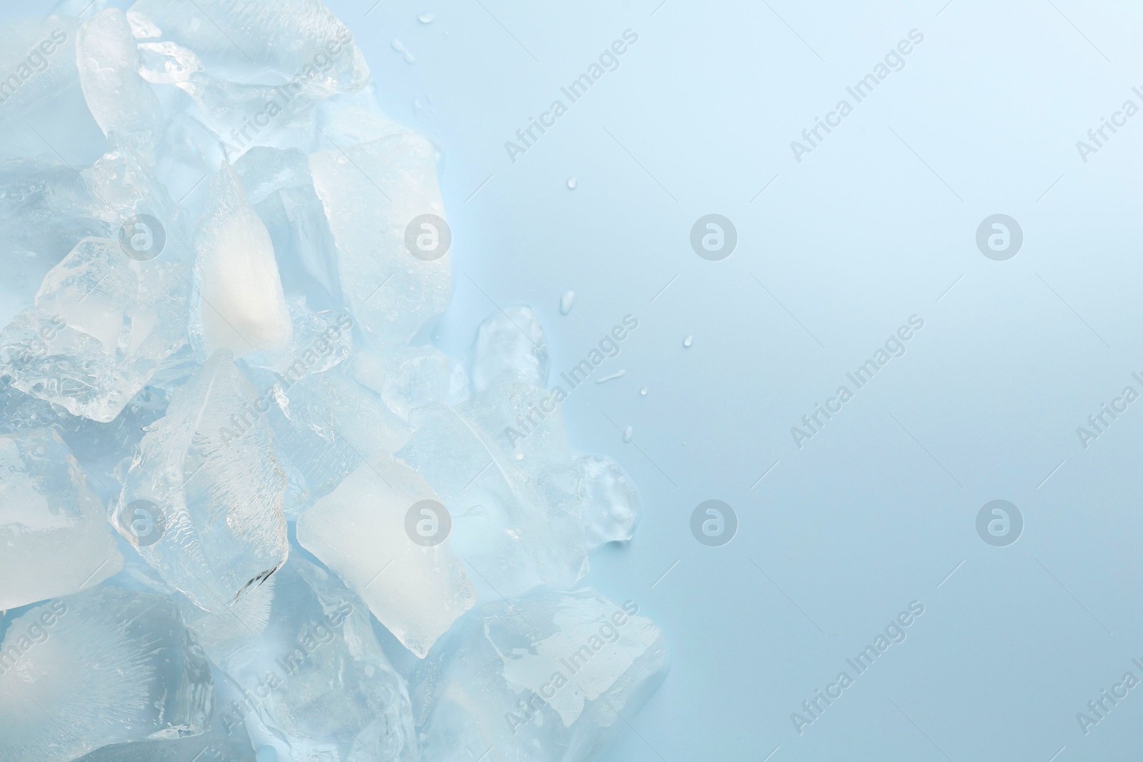 Photo of Pieces of crushed ice on light blue background, top view. Space for text