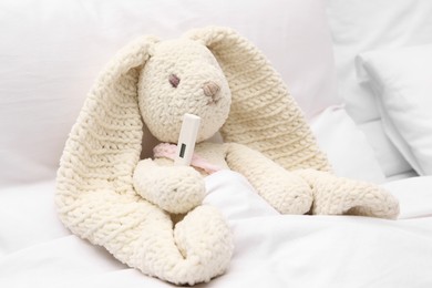Photo of Toy cute bunny with thermometer under blanket in bed