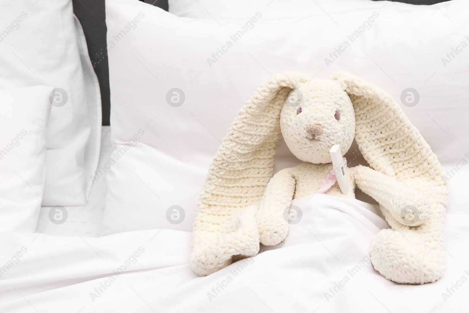 Photo of Toy cute bunny with thermometer under blanket in bed