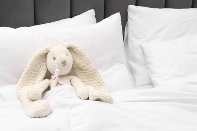 Photo of Toy cute bunny with thermometer under blanket in bed