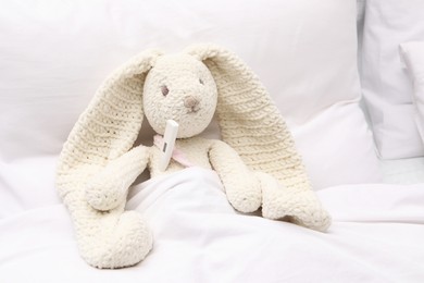 Photo of Toy cute bunny with thermometer under blanket in bed