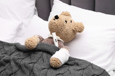 Toy cute bear with bandage and thermometer under blanket in bed