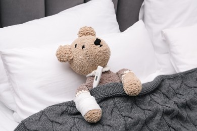 Photo of Toy cute bear with bandage and thermometer under blanket in bed