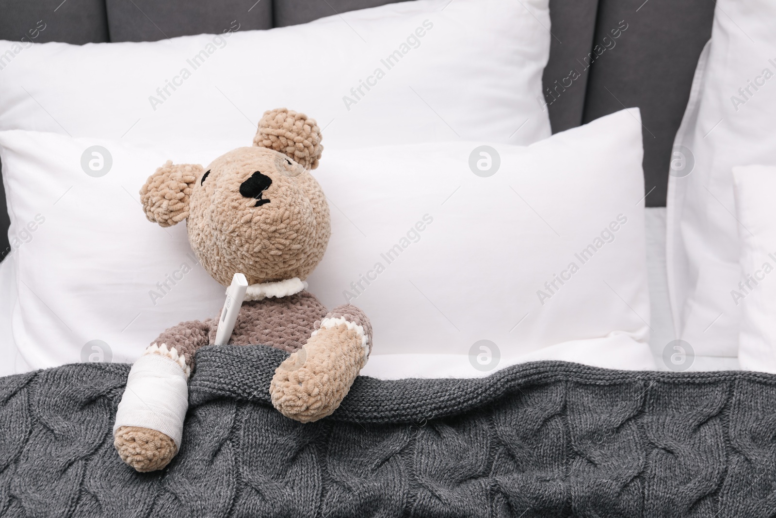 Photo of Toy cute bear with bandage and thermometer under blanket in bed