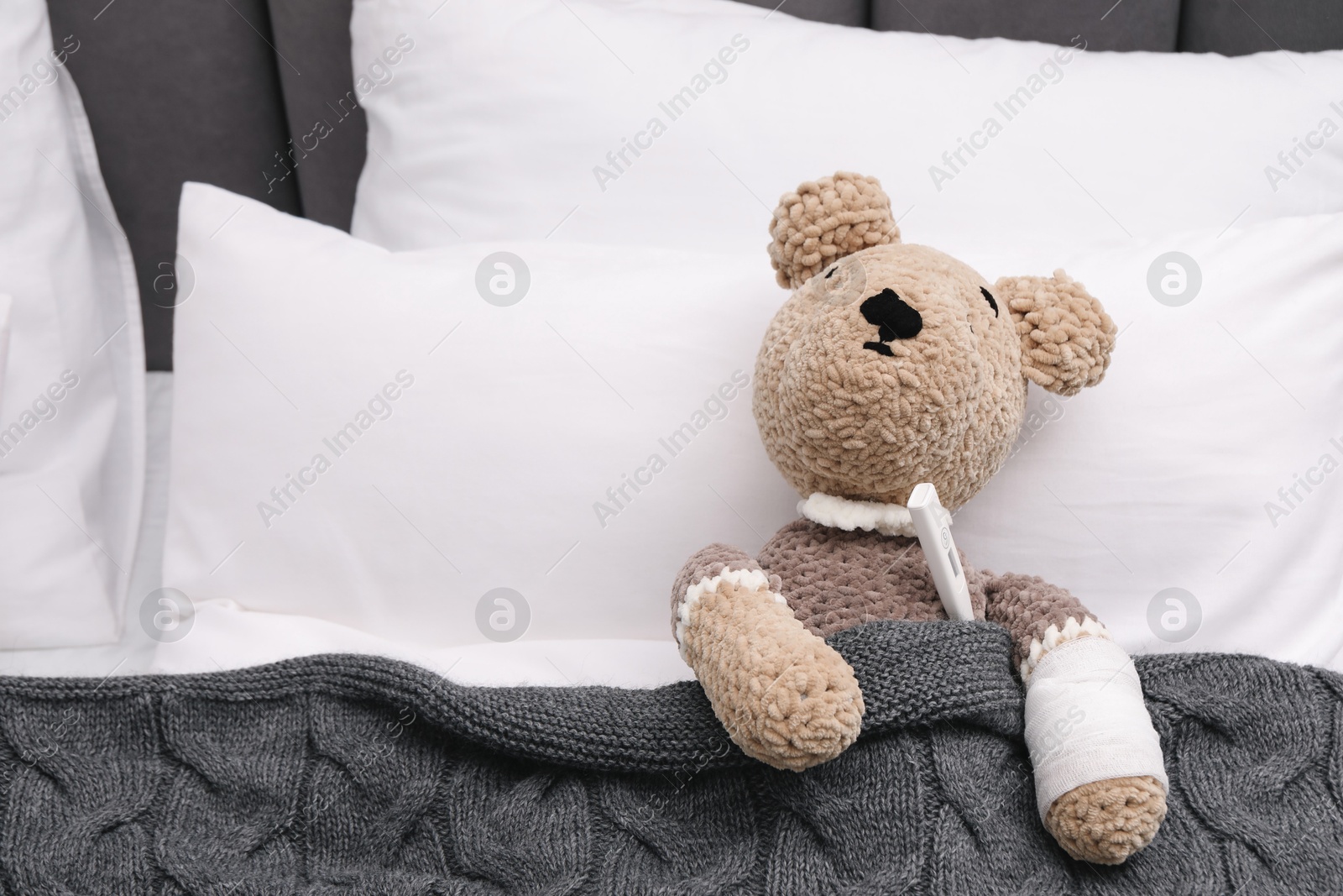 Photo of Toy cute bear with bandage and thermometer under blanket in bed