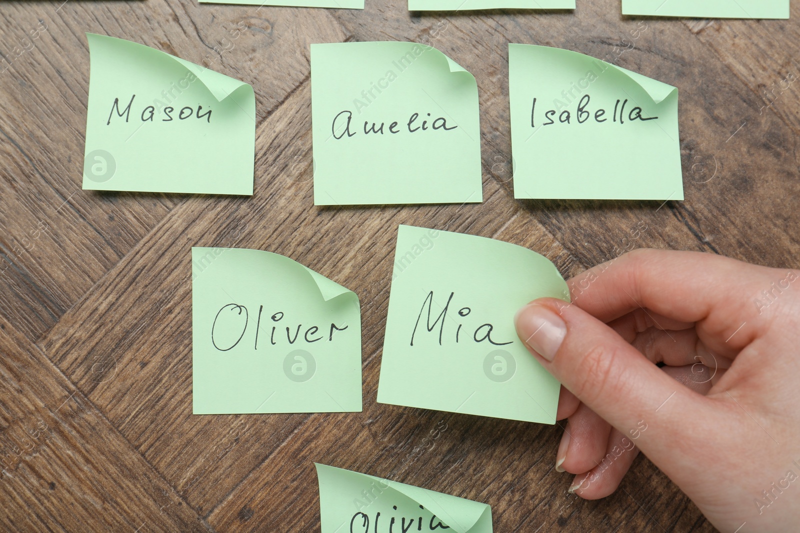 Photo of Woman holding paper sticker with name at wooden table, top view. Choosing baby's name