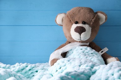 Photo of Toy bear with thermometer under blanket near blue wooden wall, space for text