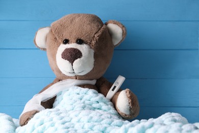 Toy bear with thermometer under blanket near blue wooden wall