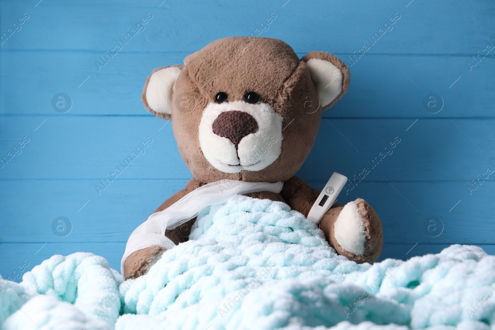 Photo of Toy bear with thermometer under blanket near blue wooden wall