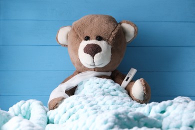 Toy bear with thermometer under blanket near blue wooden wall