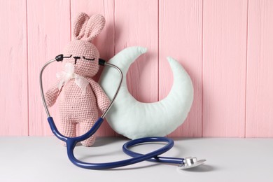 Toy bunny with stethoscope and pillow on light table near pink wooden wall