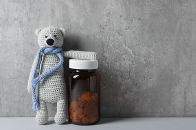 Toy bear and bottle of pills on light table near grey wall, space for text